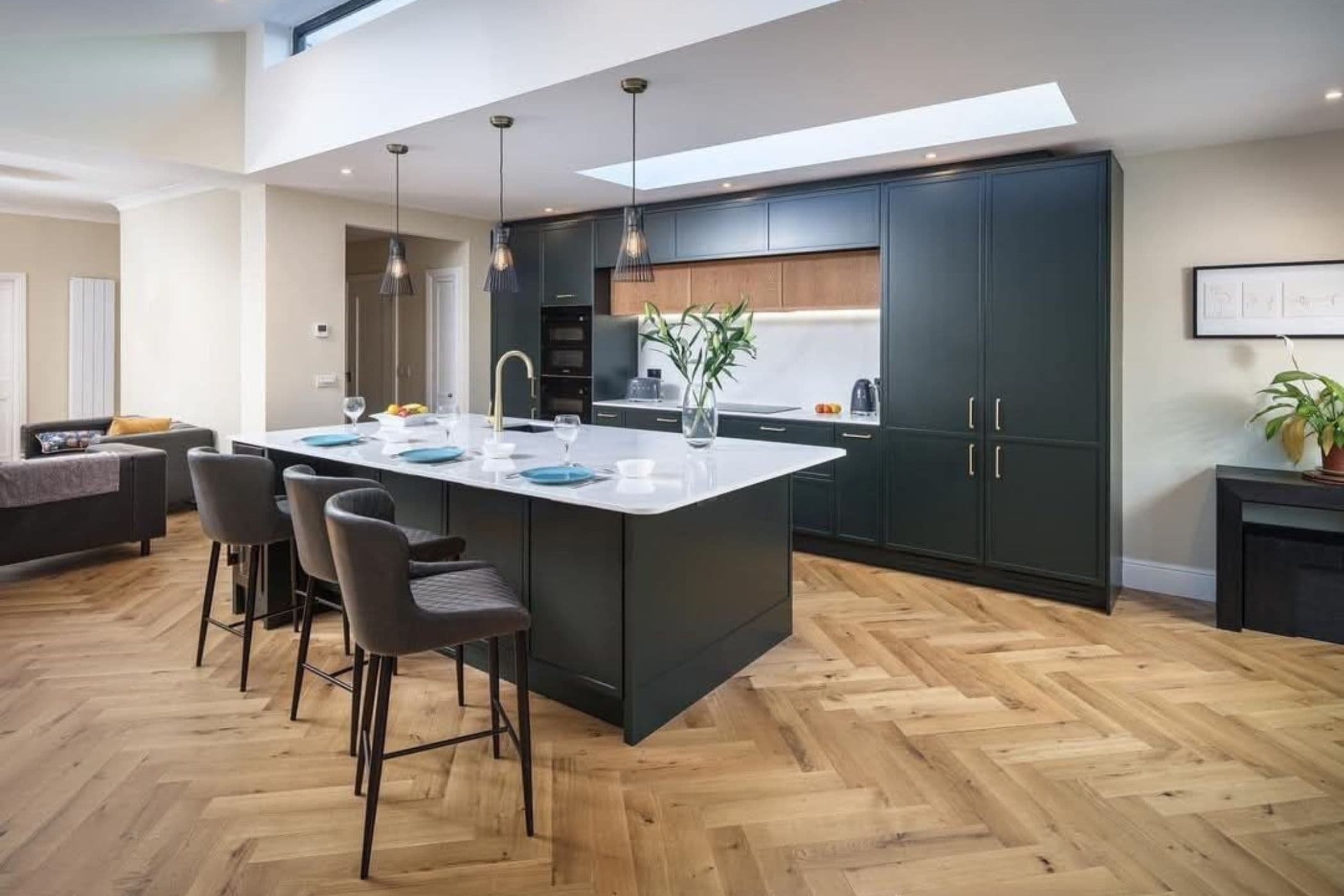 Dark green shaker kitchen with a white island, pendant lights and herringbone oak floor
